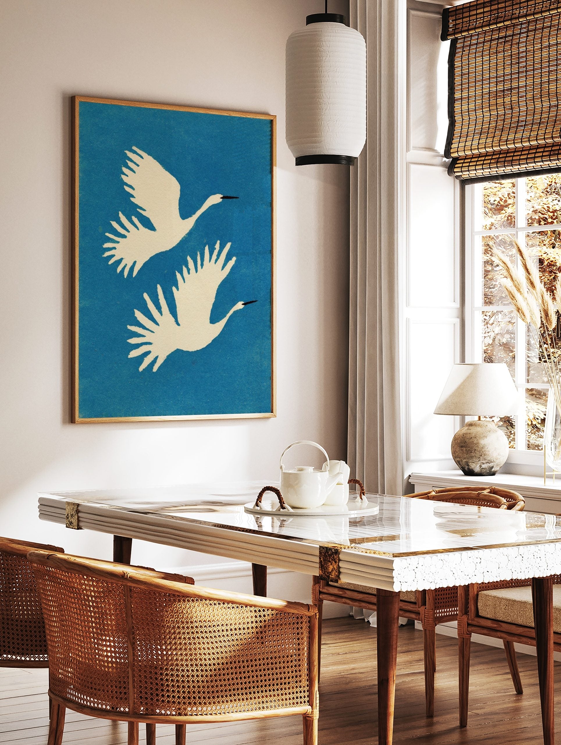Two white cranes with black beaks flying upwards against a blue, textured background in a, in a styled room mockup