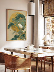 White crane standing on a pine tree branch against a large golden moon and teal-green foliage art, in a styled room mockup