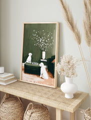 Illustrative print of two white dogs playing chess on a green ottoman with flowers in a vase, in an alternate framed mockup