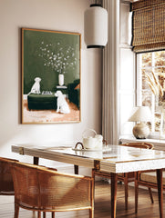 Illustrative print of two white dogs playing chess on a green ottoman with flowers in a vase, in a styled room mockup