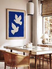Two white illustrative doves flying against a deep blue background with a beige border, minimalist, in a styled room mockup