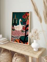 Illustrative print of a white duck at a dining table with candles, flowers, wine glasses, and, in an alternate framed mockup