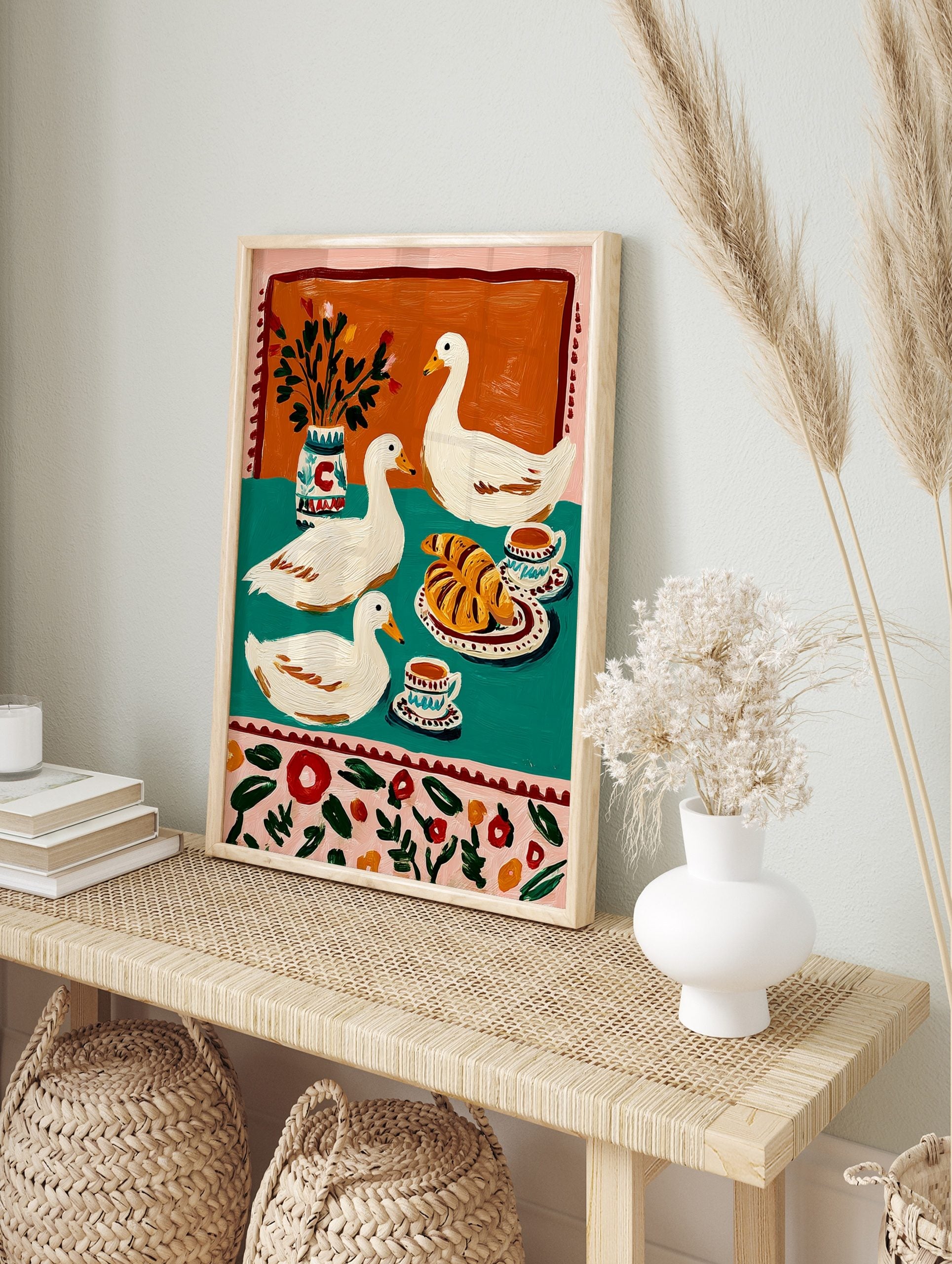 Illustrative print of three white ducks with croissants, coffee, and a vase on a teal and, in an alternate framed mockup