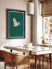 White egret bird illustration in flight against a teal green background with cream and navy borders, in a styled room mockup