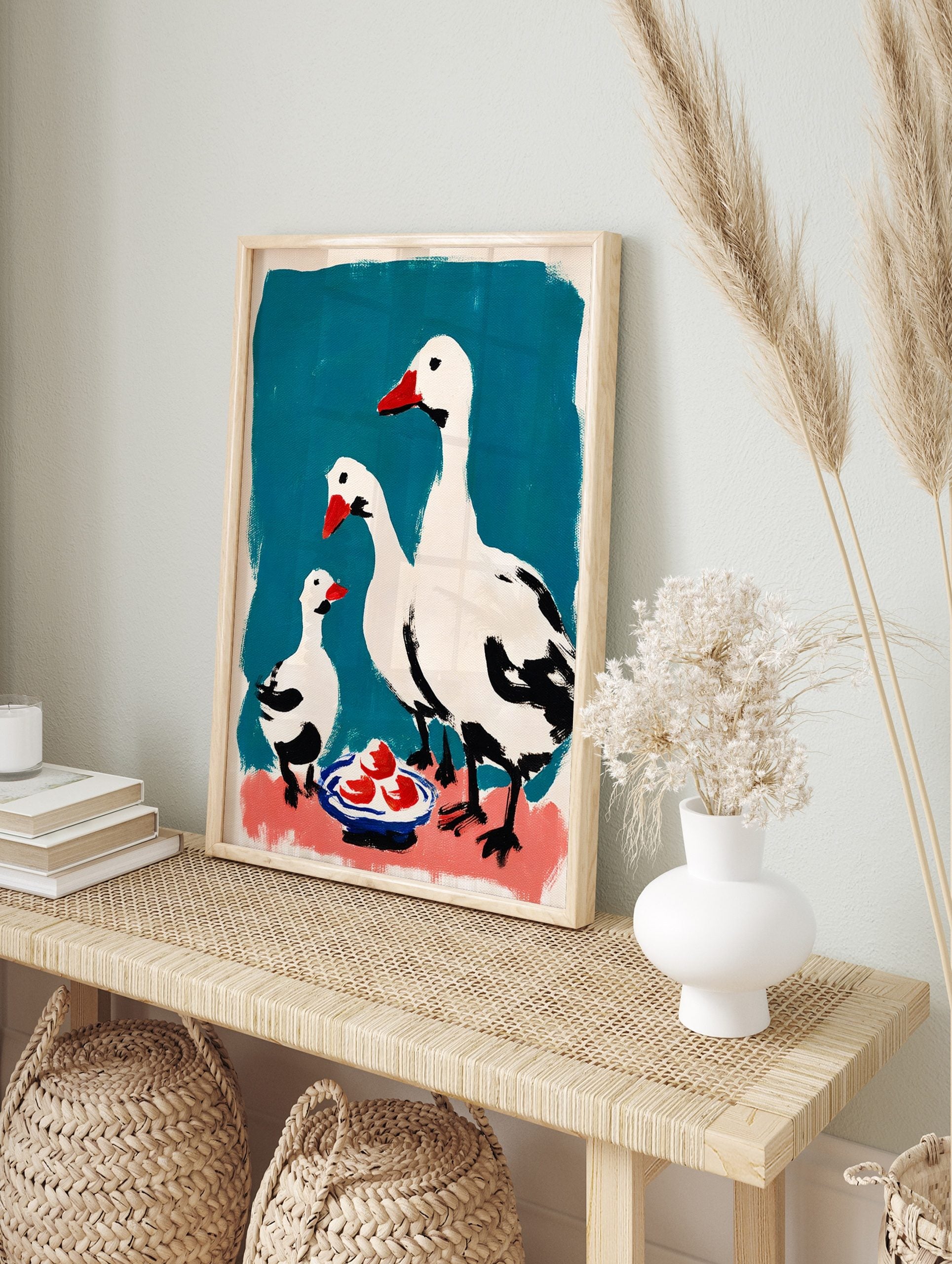 White geese family wall art with red beaks and black details on teal and pink background with, in an alternate framed mockup