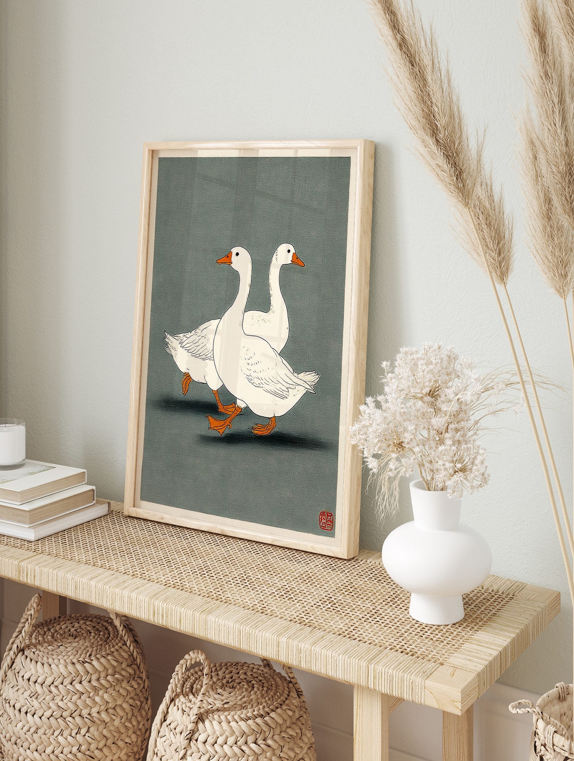 Two white geese with orange beaks and feet walking in profile on a dark grey-green, in an alternate framed mockup