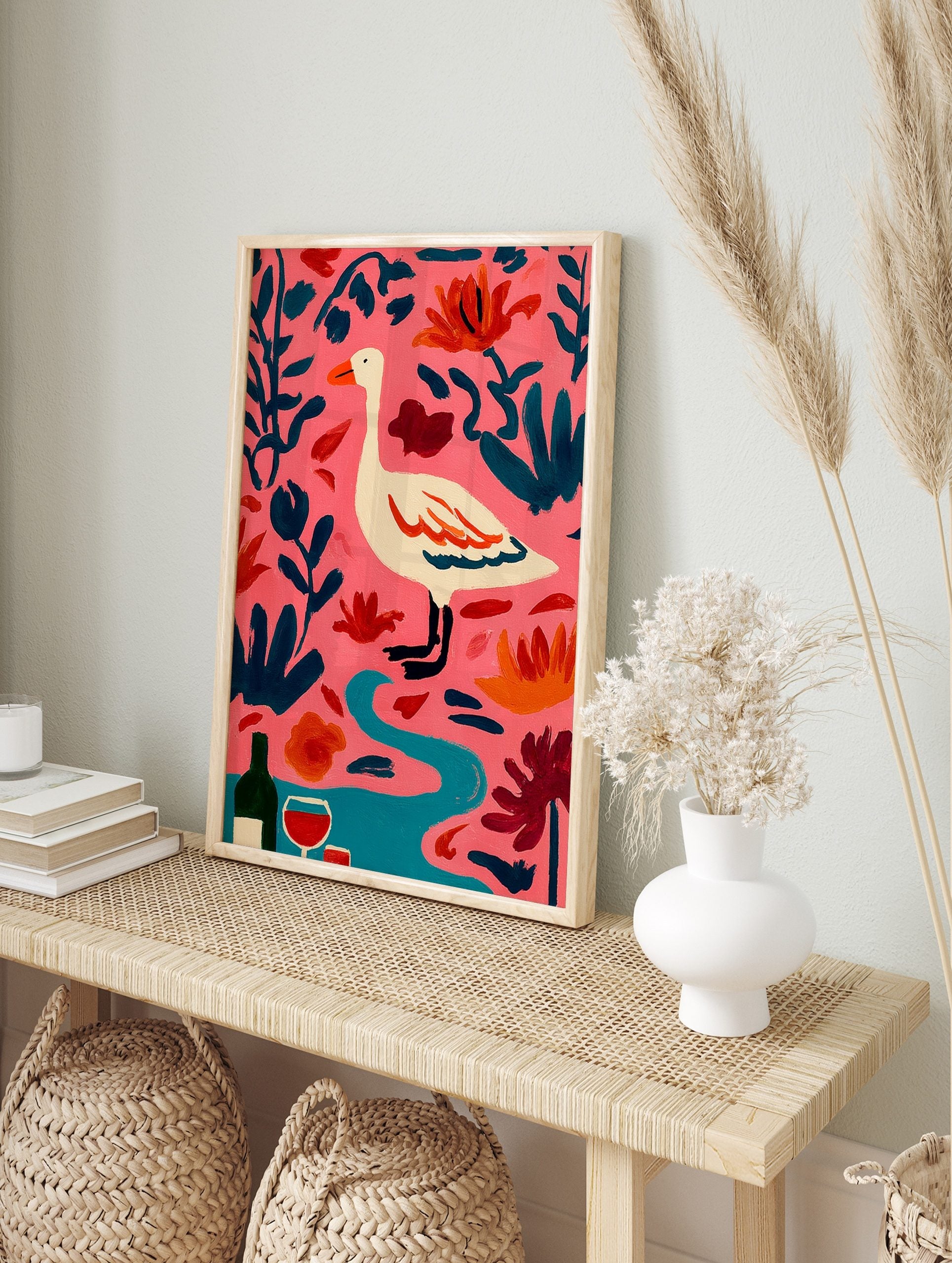 Illustrative white goose with orange beak, pink background, dark teal leaves, orange flowers, in an alternate framed mockup