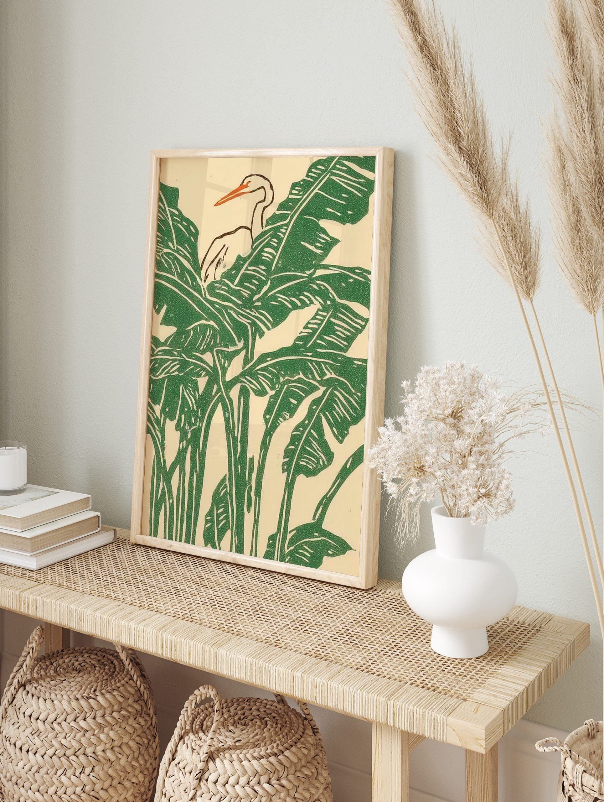 White heron with orange beak amidst green tropical banana leaves in an illustrative print, in an alternate framed mockup