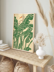 White heron with orange beak amidst green tropical banana leaves in an illustrative print, in an alternate framed mockup