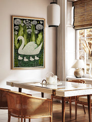 Illustrative white swan and four cygnets swimming in green water, surrounded by green reeds and, in a styled room mockup