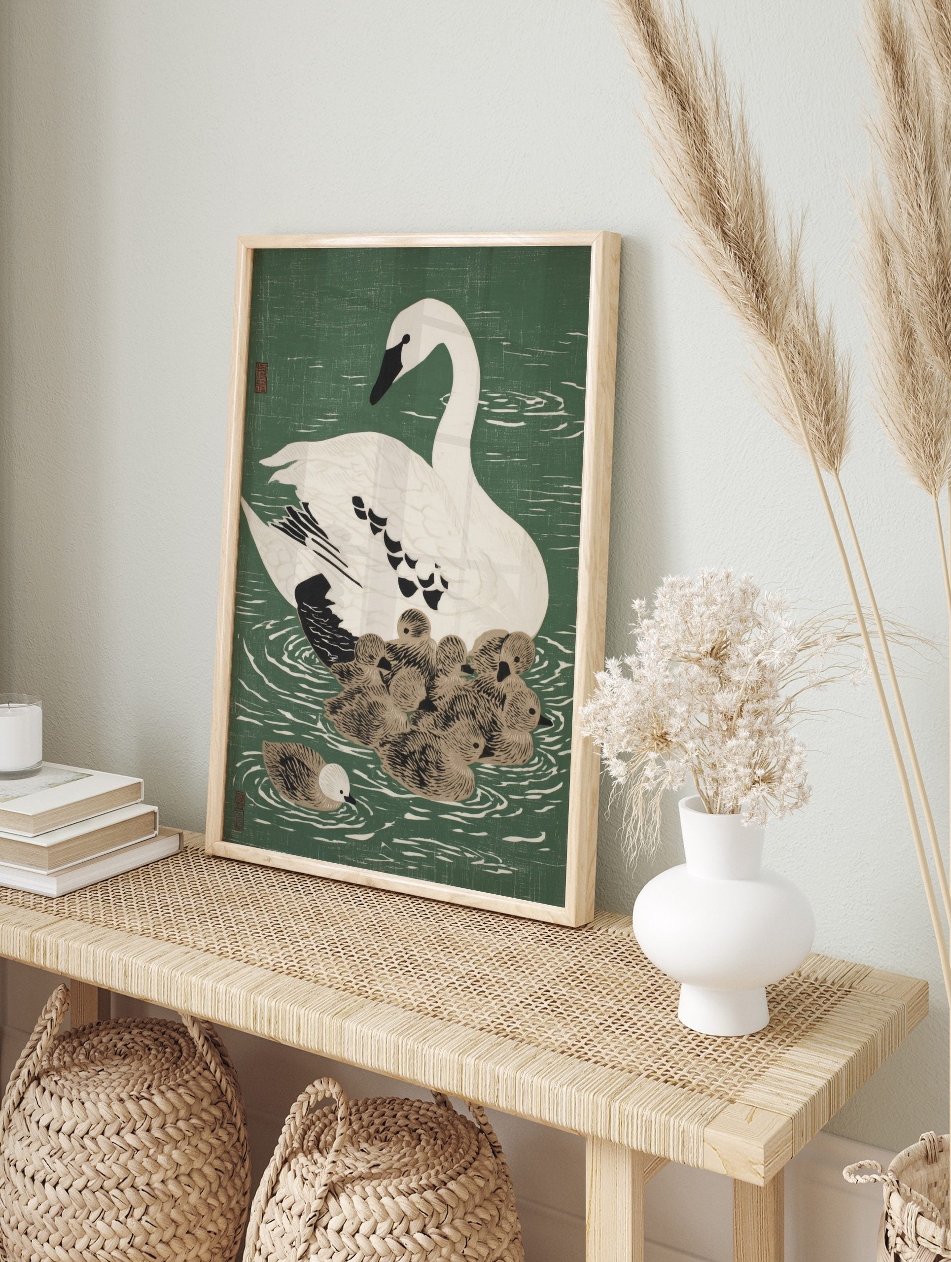 White swan with black beak and eye swimming with a cluster of brown cygnets on green water, in an alternate framed mockup