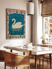 Illustrative white swan with yellow beak swimming in blue water, framed by a pale pink botanical, in a styled room mockup