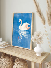 White swan with orange beak floating on textured blue water, with its reflection visible below, in an alternate framed mockup