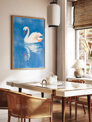 White swan with orange beak floating on textured blue water, with its reflection visible below, in a styled room mockup
