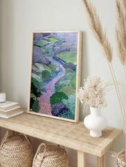 Illustrative landscape art print of a winding pink path through a green valley with blue, in an alternate framed mockup