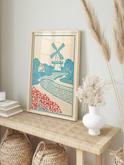 Illustrative windmill landscape art print with a bridge, cottage, and red flowers in a blue, in an alternate framed mockup