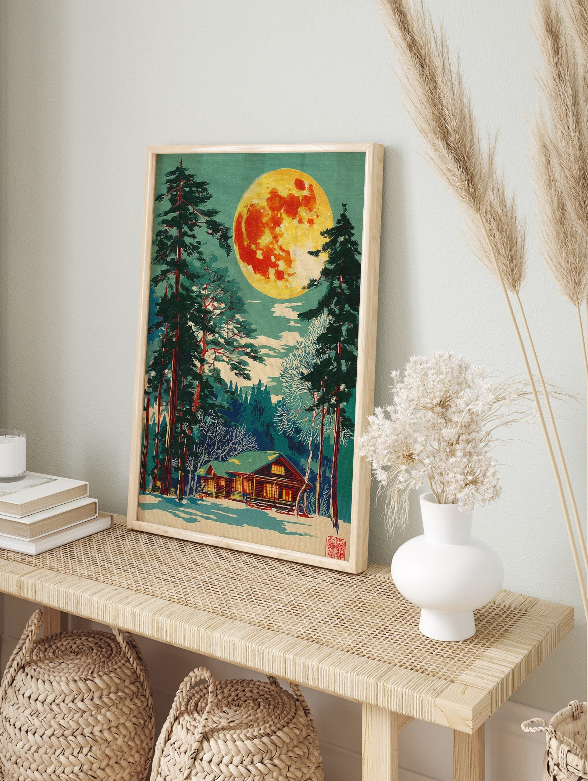 Illustrative print of a vibrant full moon over a snow-covered log cabin and tall pine trees, in an alternate framed mockup