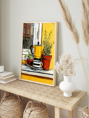 Illustrative print of a yellow moka pot and striped coffee cup with potted green plants on a, in an alternate framed mockup