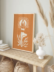 White silhouette of person in yoga tree pose with sun rays and plants on orange background, in an alternate framed mockup