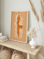 Stylised burnt orange silhouette of a woman in a yoga pose with a cream crescent moon and, in an alternate framed mockup