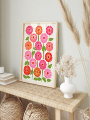 Botanical zinnia flower illustration in pink, orange, and red with green stems on a cream, in an alternate framed mockup