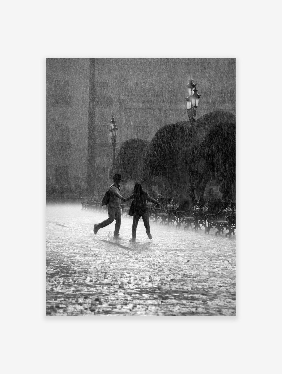 Black and white photograph of a couple holding hands and running through a heavy rainstorm in a park.
